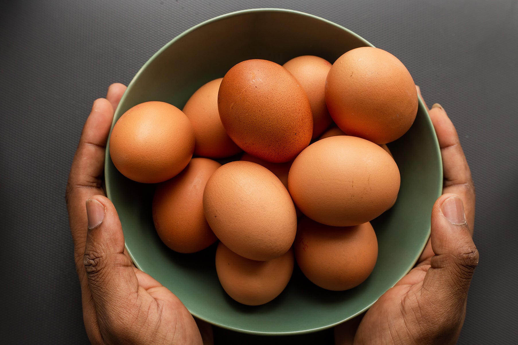 Hands holding a group of eggs in a green bowl.