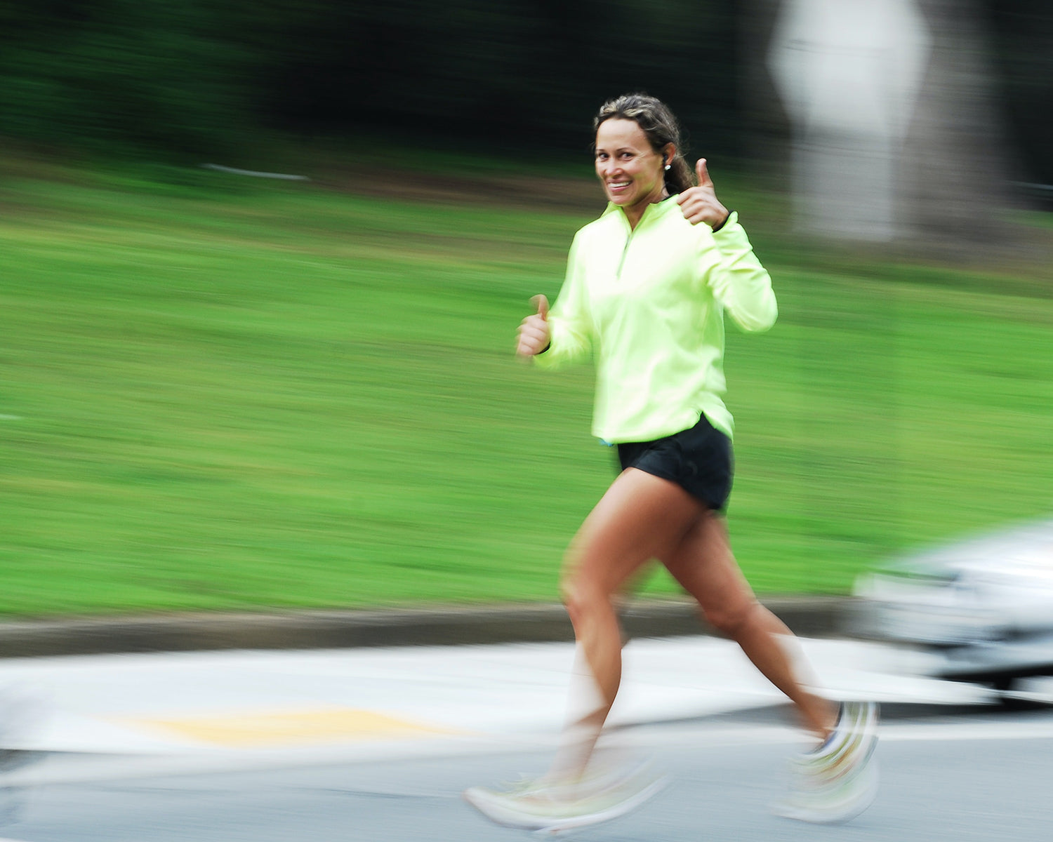 Woman smiling and giving a thumbs up sign while running.