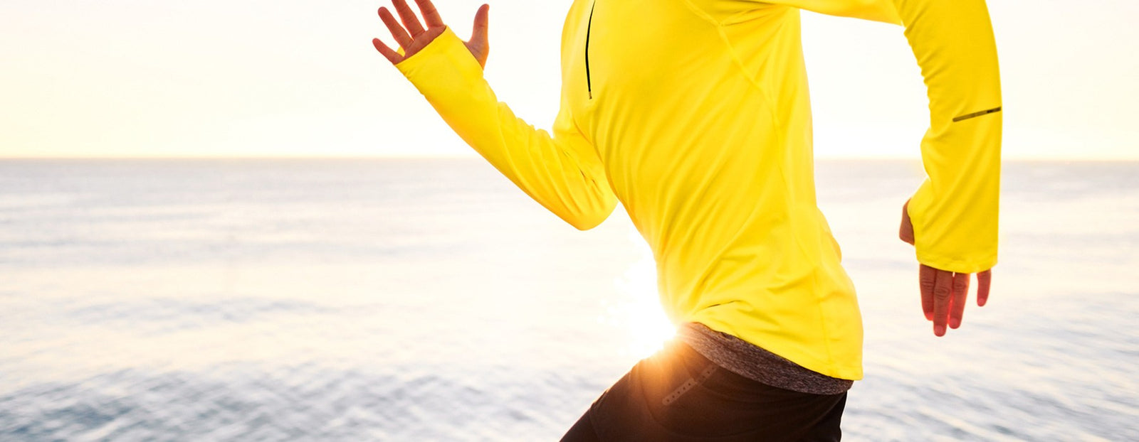 Person running near water wearing a bright yellow athletic jacket.